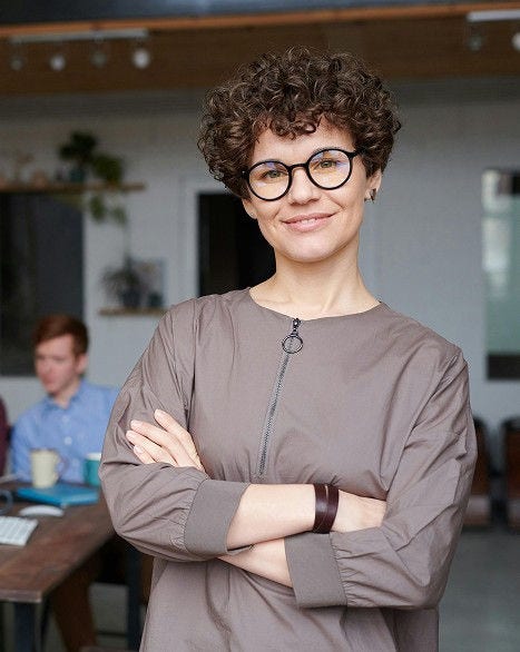 Mujer sonriente en primer plano con su equipo de trabajo al fondo en la oficina.